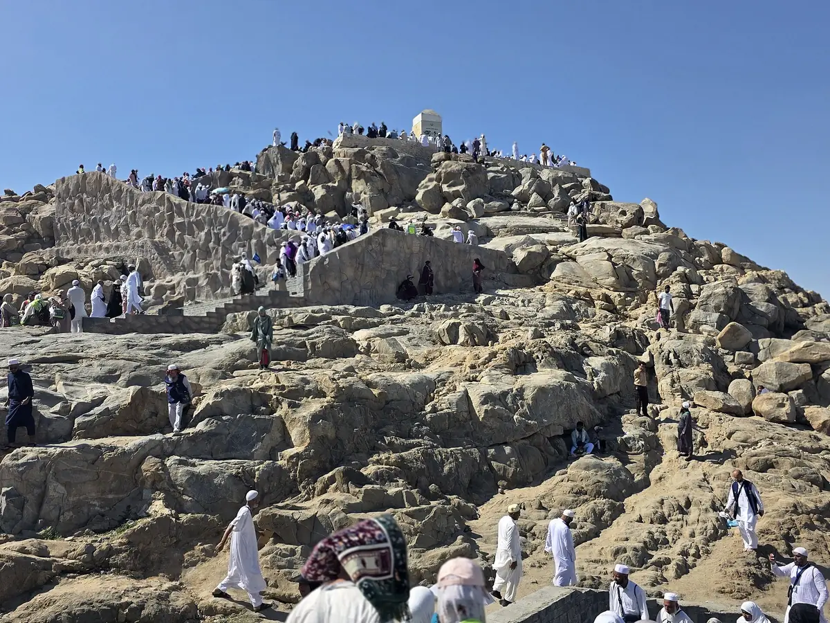 Pilgrims on the rocky slopes of Jabal ar-Rahmah at Arafat, with the white pillar on its summit
